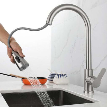Llave de lavaplatos cromada con cabezal flexible, mostrando agua en modo ducha sobre un fregadero de cocina.